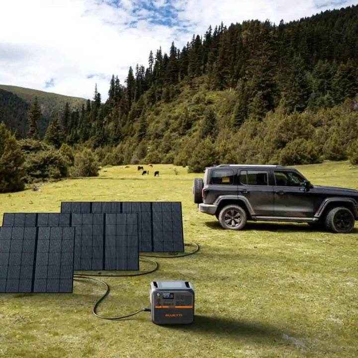 Bluetti AC200P L solar generator in use outdoors, connected to several solar panels, set against a scenic backdrop of hills and forest.