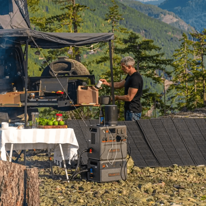 Man preparing food outdoors at a campsite with Bluetti AC240P and solar panel array powering appliances.