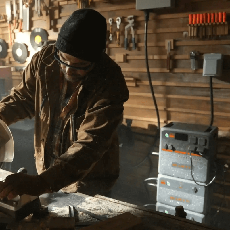Man in woodworking shop using a saw with Bluetti AC240P power stations stacked in the background.