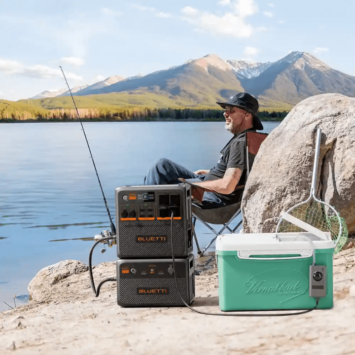 Man relaxing while fishing by a lake with a Bluetti AC240P and B210P expansion battery powering a cooler.