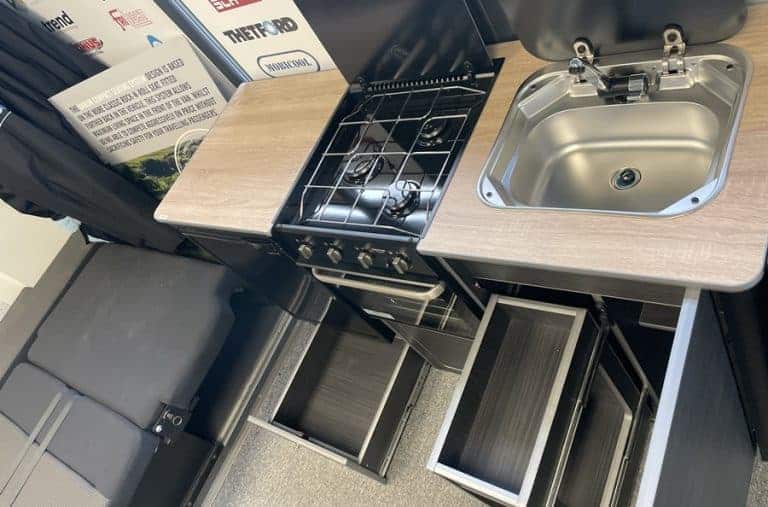 Large Campervan Kitchen Pod top view showing gas hob, stainless steel sink, and extended storage drawers in indoor display area.