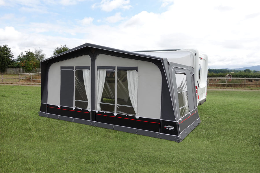 Camptech Mayfair DL caravan awning attached to a white caravan on a grassy campsite with cloudy sky background.