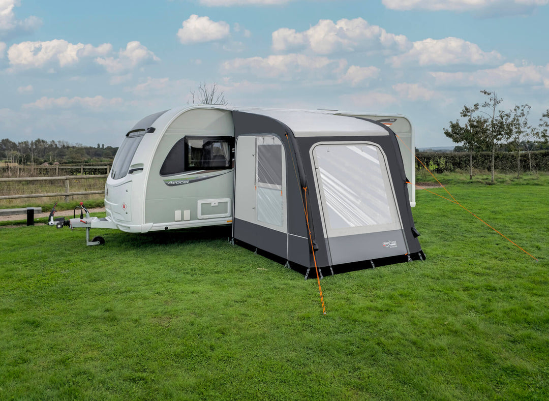 Camptech Starline 200 inflatable caravan awning beside a white Avocet caravan on a green campsite with cloudy sky background.