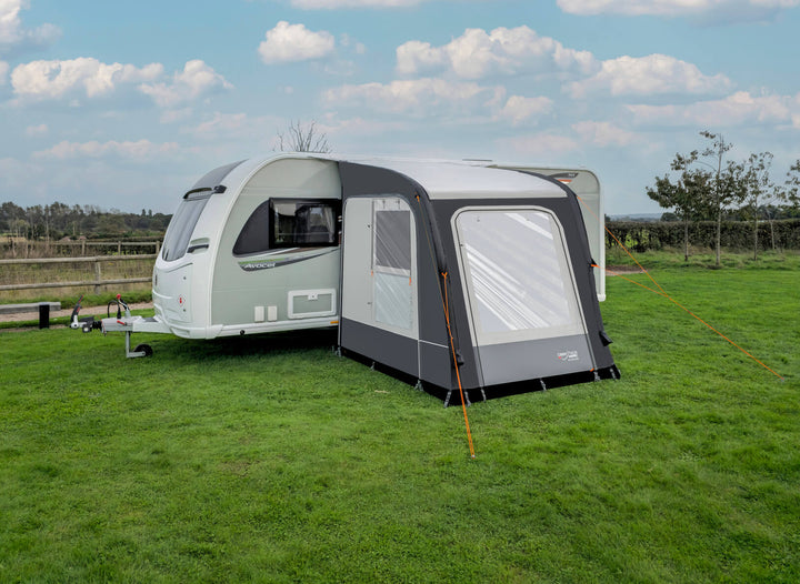 Camptech Starline 200 inflatable caravan awning beside a white Avocet caravan on a green campsite with cloudy sky background.