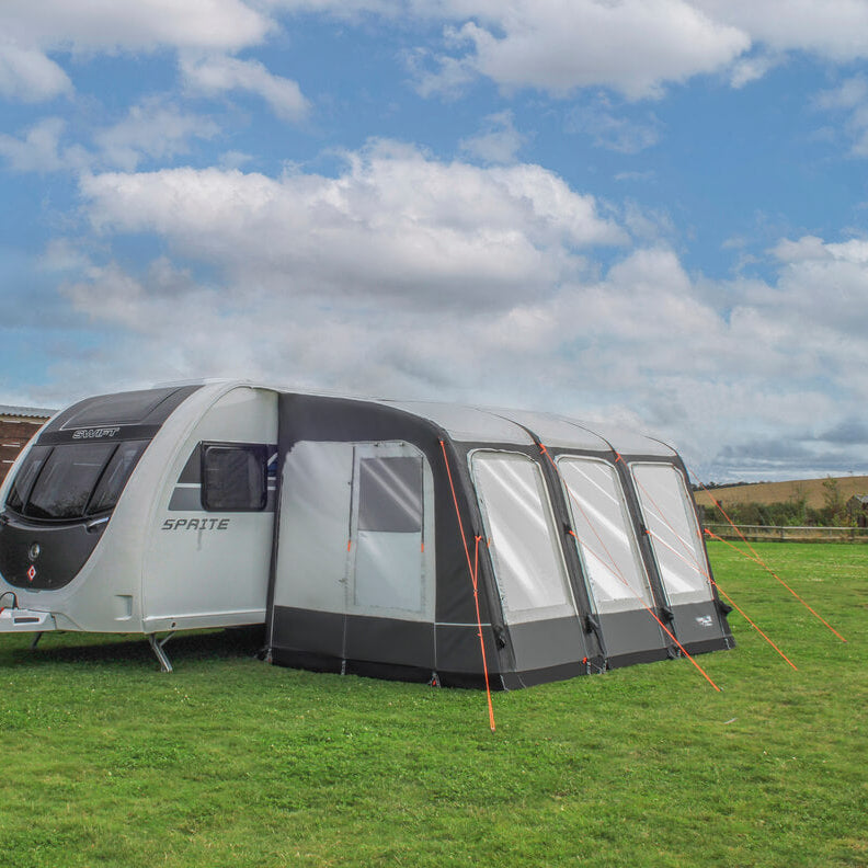 Camptech Starline 390 caravan awning attached to a white Sprite caravan on a grassy campsite with cloudy blue sky background.