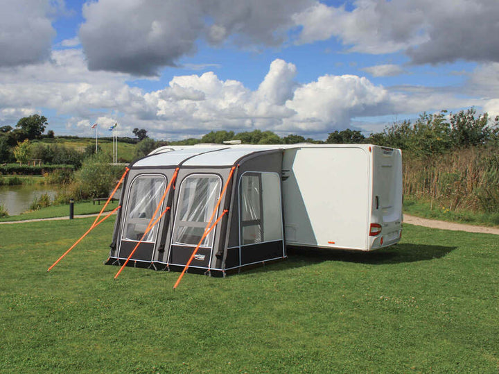 Camptech Starline Elite 260 air awning beside a white caravan near a lakeside campsite under cloudy skies.