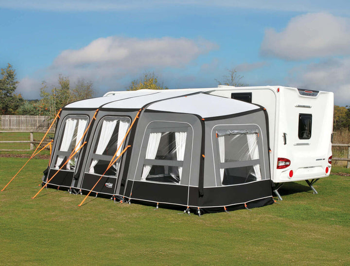 Camptech Starline Elite Infinity awning connected to a white Swift caravan on a sunny grassy campsite with blue sky background.