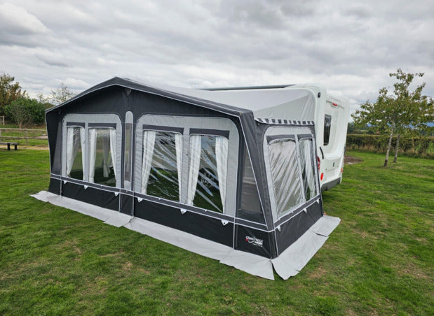 Camptech Westminster CS caravan awning with privacy blinds closed beside a white caravan on a grassy campsite.
