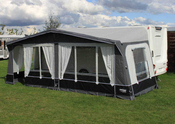Camptech Kensington Air full-size caravan awning with side door and panoramic windows, pitched on a grassy field beside a caravan under a cloudy sky.