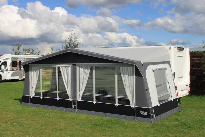 Camptech Kensington Air awning with white curtains and clear panels, attached to a Swift caravan on green grass at a sunny campsite.