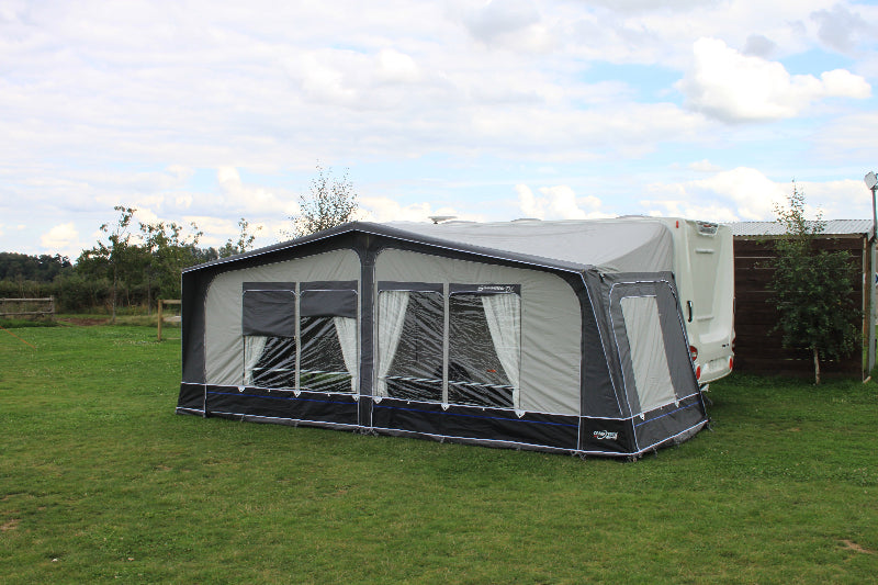 Camptech Savanna DL full caravan awning with clear windows and curtains, attached to a white caravan on green grass under a partly cloudy sky.
