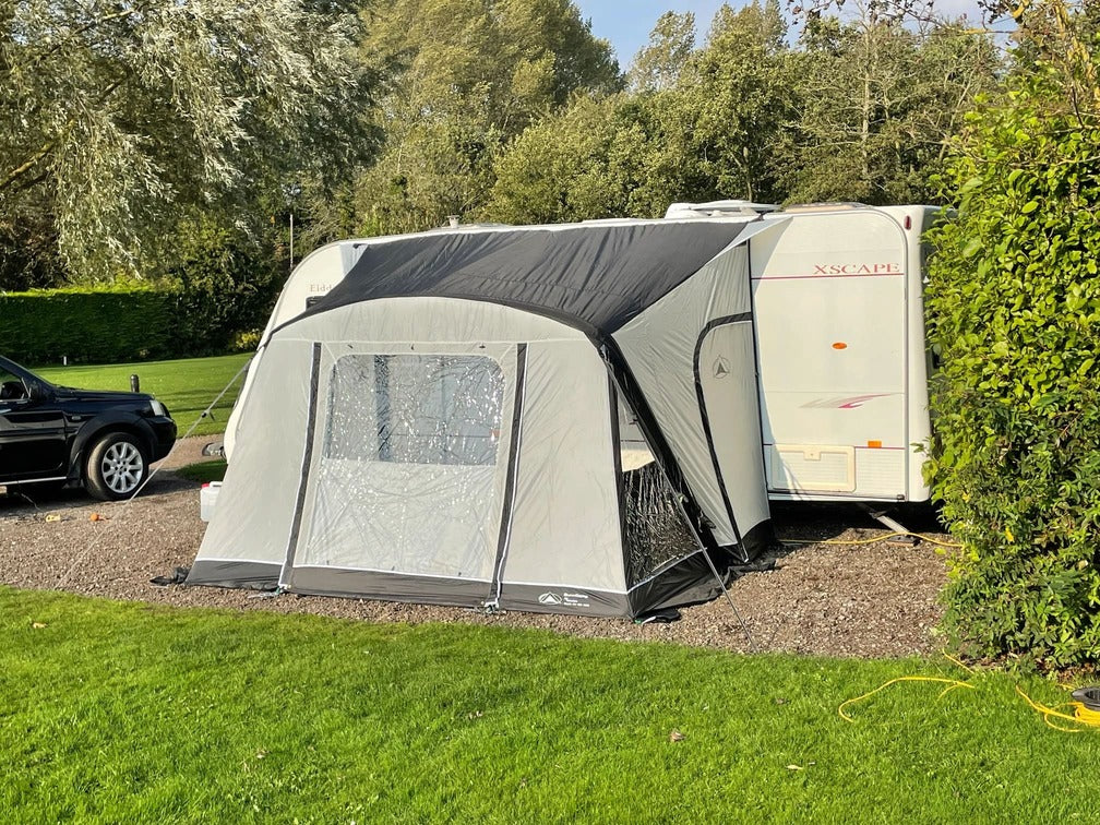 SunnCamp Dash Air 260 SC awning attached to a white caravan, featuring grey and black fabric panels, a clear front window, and a compact enclosed entrance on a gravel campsite.