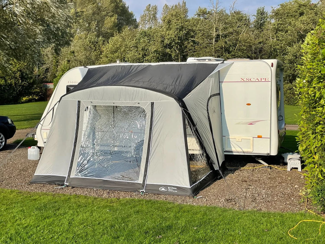 SunnCamp Dash Air 260 SC awning with its front panels closed, attached to a white caravan surrounded by green grass and trees.