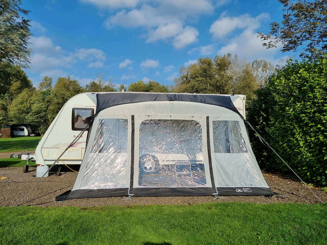 SunnCamp Dash Air 390 SC caravan awning with a wide transparent front window, grey fabric panels and black roof, attached to a white caravan on a sunny campsite.
