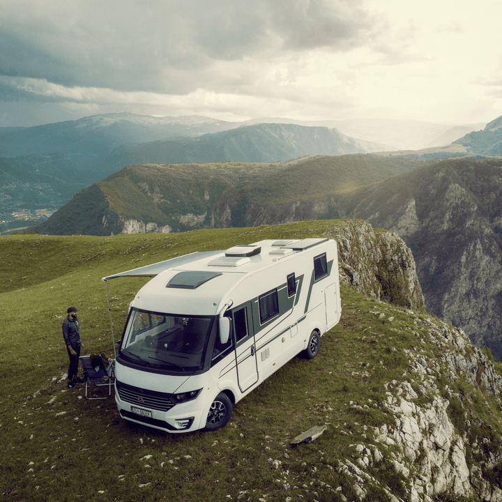 Wide-angle shot of a motorhome parked near a cliff edge, equipped with the Dometic FreshJet unit on the roof; one person stands nearby with mountains in the distance.