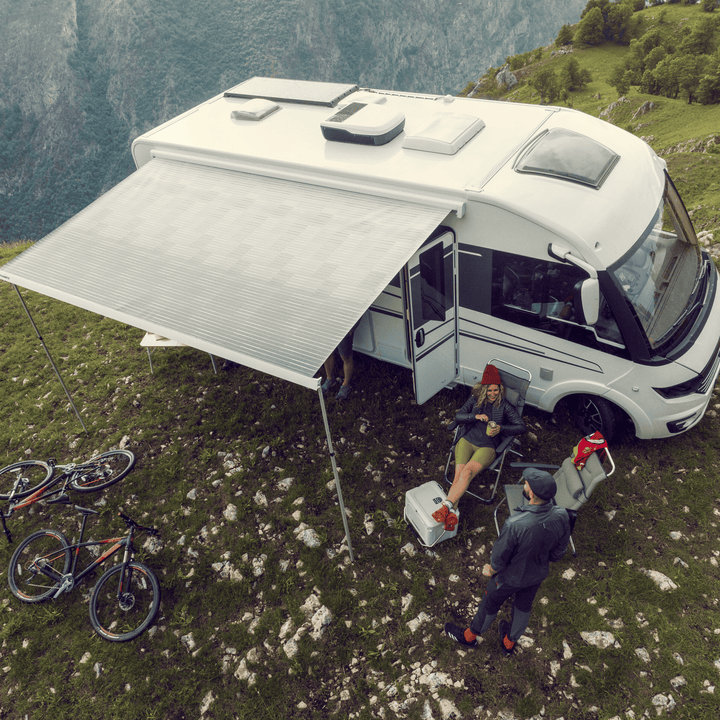 Overhead photo of a camper van parked on a grassy mountain ridge with the Dometic FreshJet unit installed on the roof; two people relaxing under the awning with mountain bikes nearby.