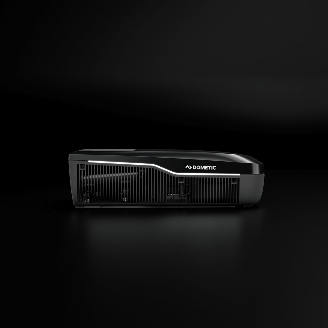 Side profile of the Dometic FreshJet FJX7 2200 in black, displaying its curved front, ventilation slots, and LED accent line, on a black background.