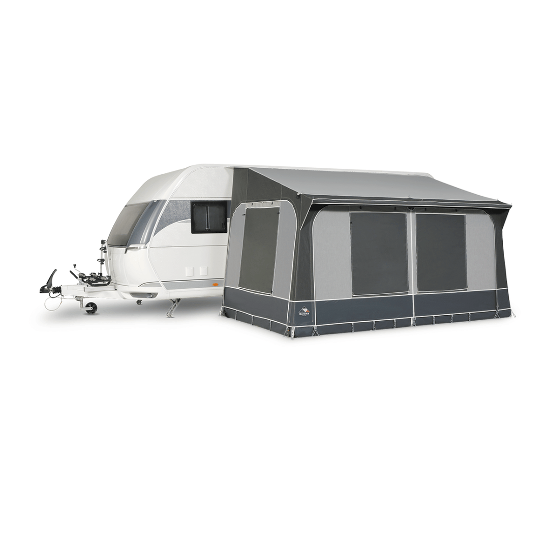 Dorema Quartz 330 Deluxe attached to a white touring caravan, featuring enclosed grey panels, large tinted windows, and a full-length canopy on a white background.