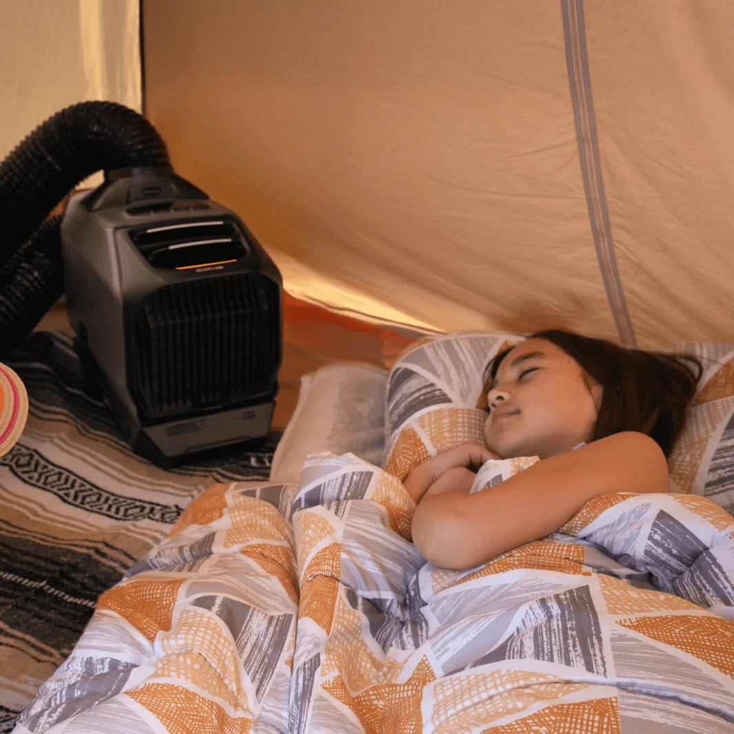 EcoFlow WAVE 3 air conditioner operating inside a tent, placed beside a sleeping child wrapped in a patterned blanket.