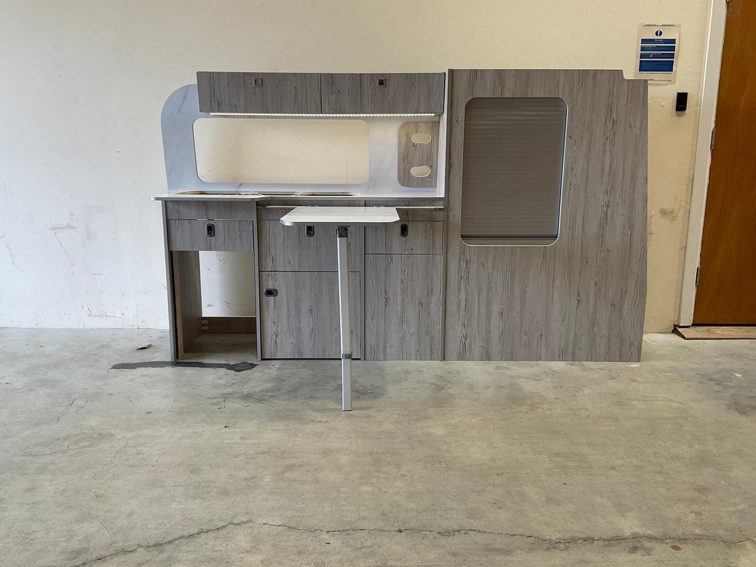 Ford Transit Custom Campervan Kitchen Unit Bespoke in gloss white and charcoal two-tone design with fold-out table and side tambour door, displayed on a concrete floor with plain wall background.