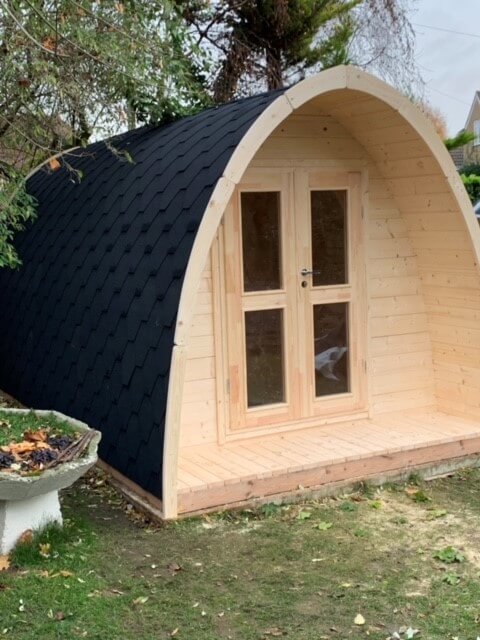 Front view of InMedias Camping Pod 480 at dusk, with double glass doors open and wooden floor illuminated by a light.