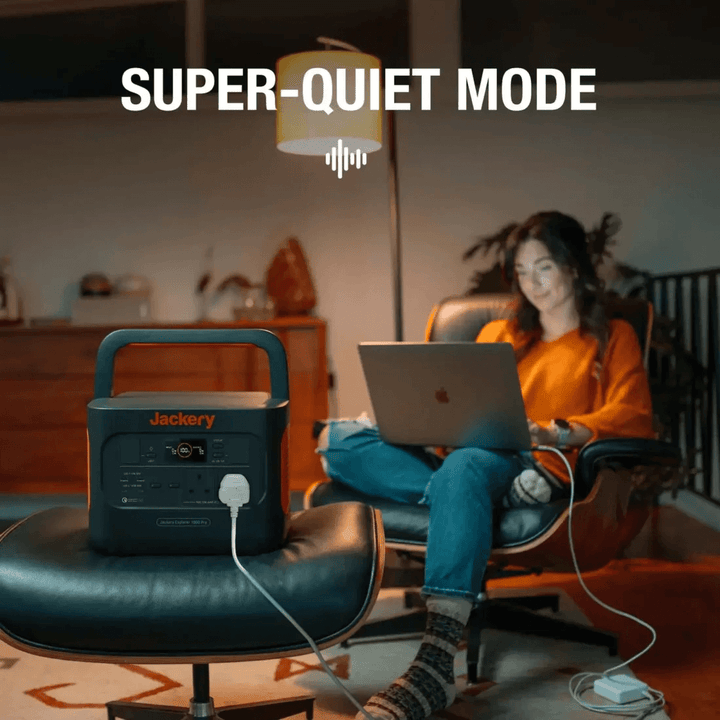 Woman using laptop indoors with Jackery Explorer 1000 Pro running silently beside her, living room background.