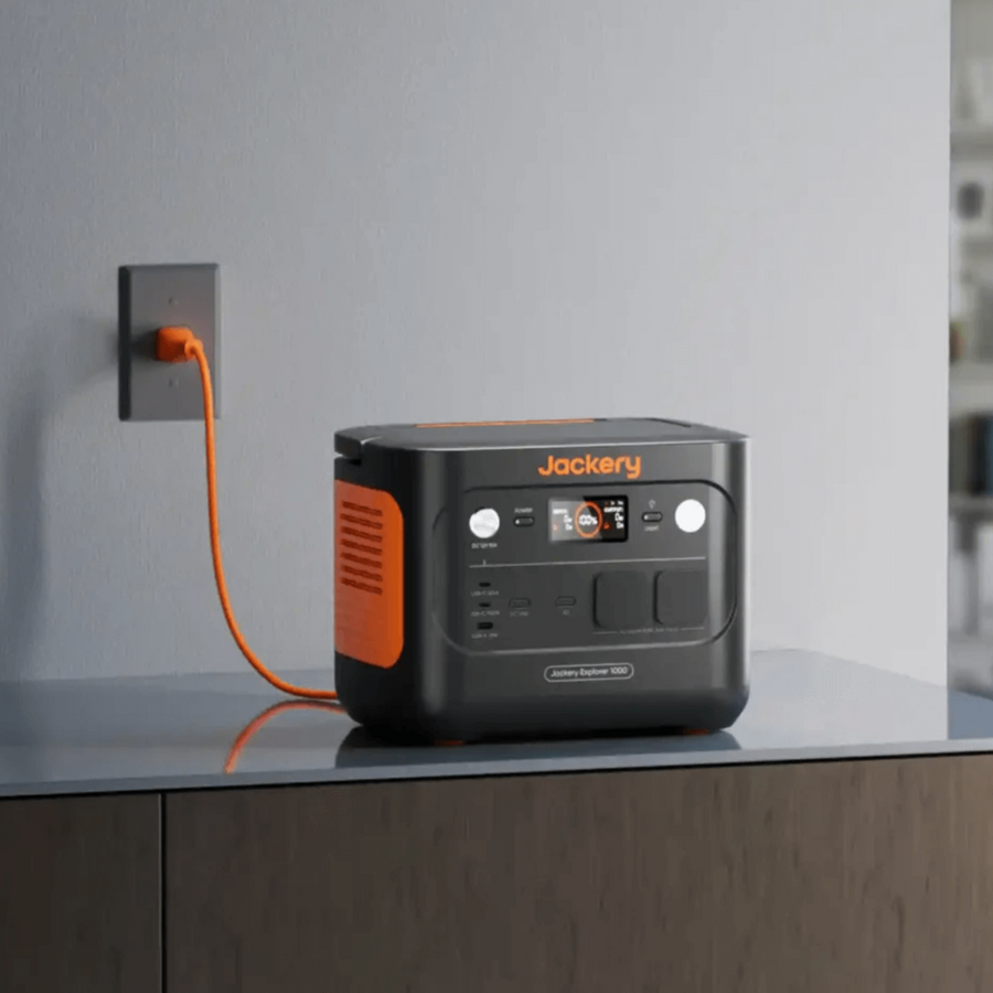 Jackery Explorer 1000 V2 charging indoors on a countertop against a grey wall.