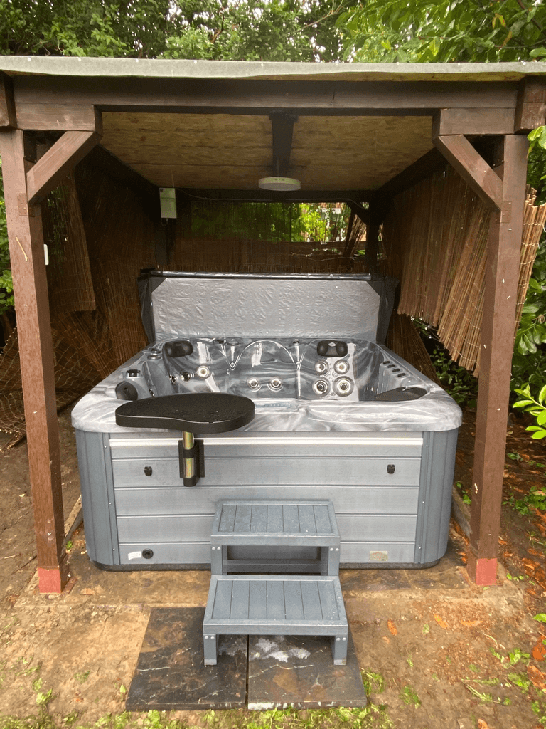 Luso Spas The Aquarius Plug & Play Hot Tub installed under a wooden gazebo with grey steps and side table on an outdoor background.