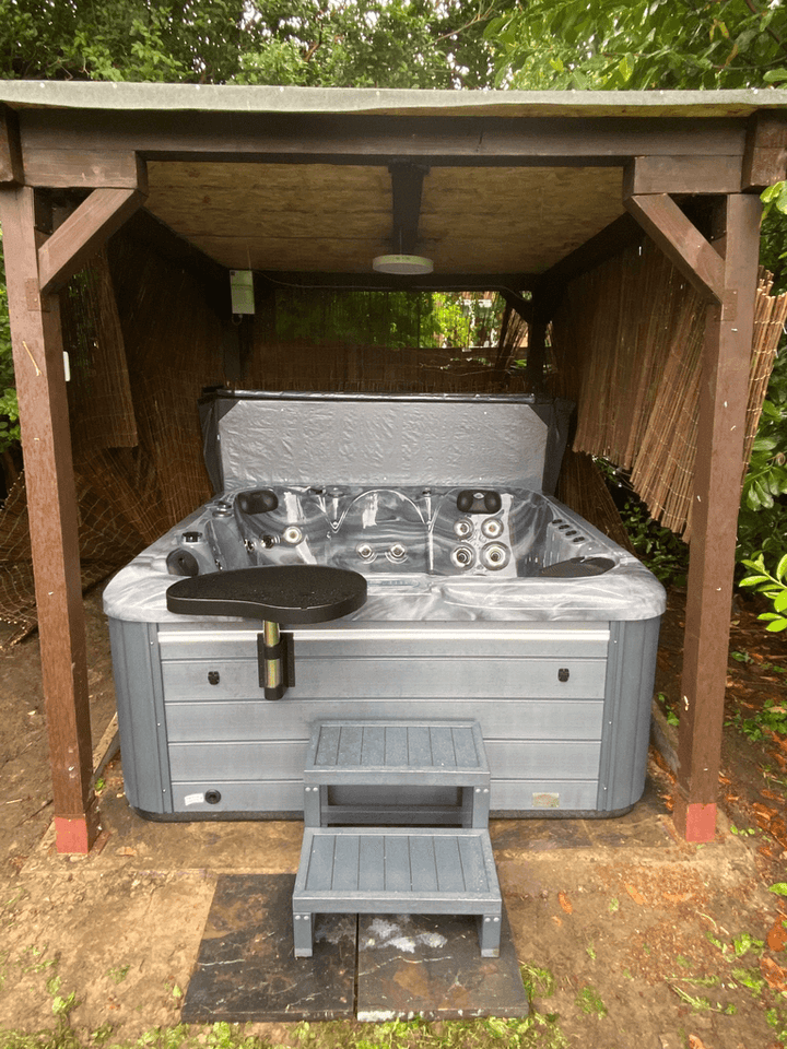 Luso Spas The Aquarius Plug & Play Hot Tub installed under a wooden gazebo with grey steps and side table on an outdoor background.