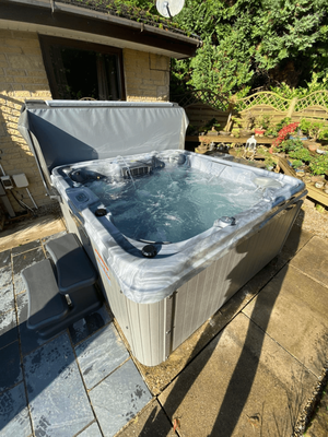 Luso Spas The Venice Hot Tub installed beside a brick house with bubbling water and grey steps on a stone patio.