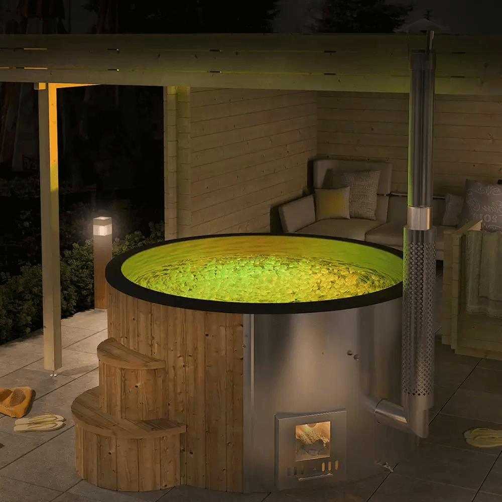 InMedias Delux 200 Hot Tub with glowing green LED-lit water, placed on a tiled patio at night under a pergola.