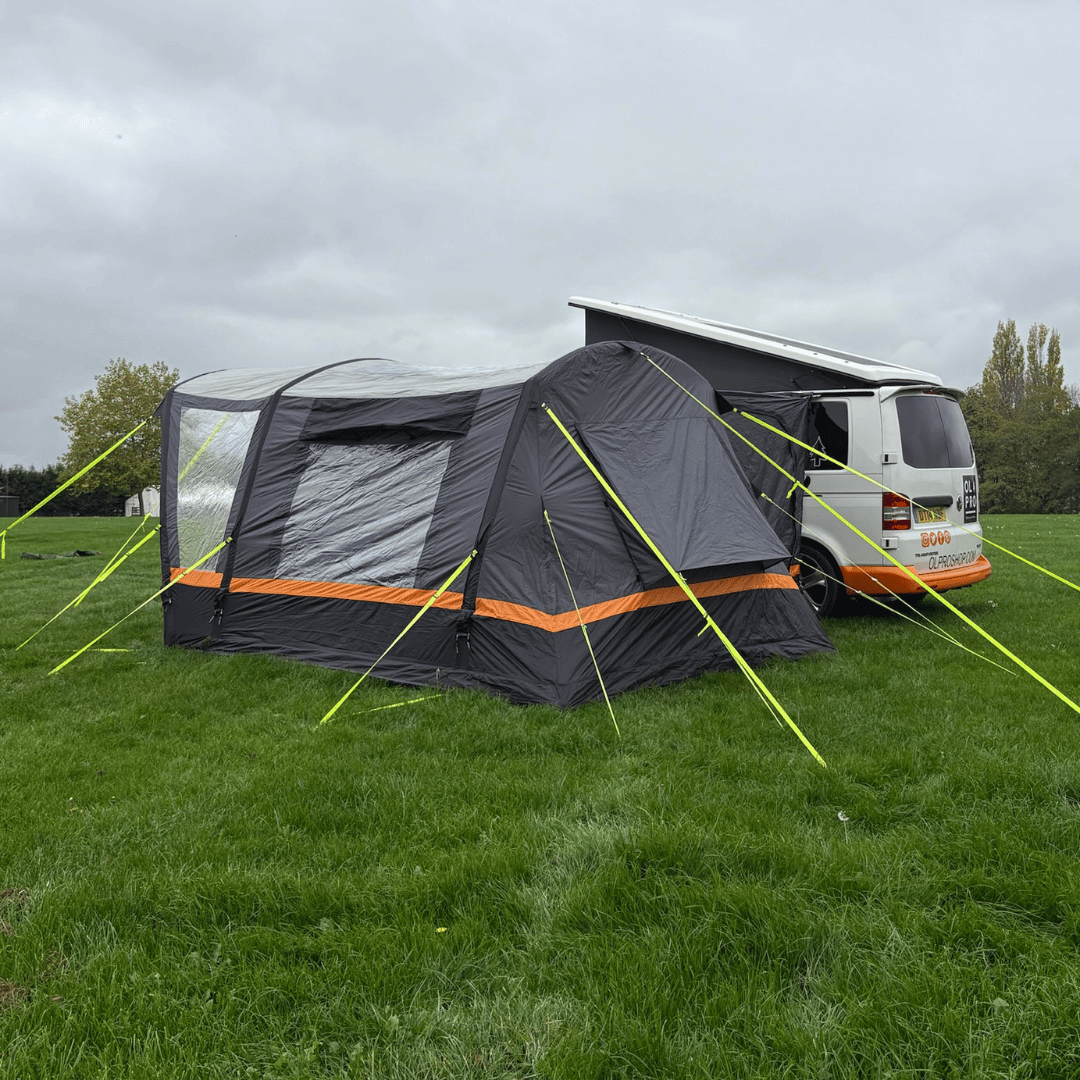 Side view of the OLPRO Hanley Breeze driveaway awning connected to a campervan on a grassy field.