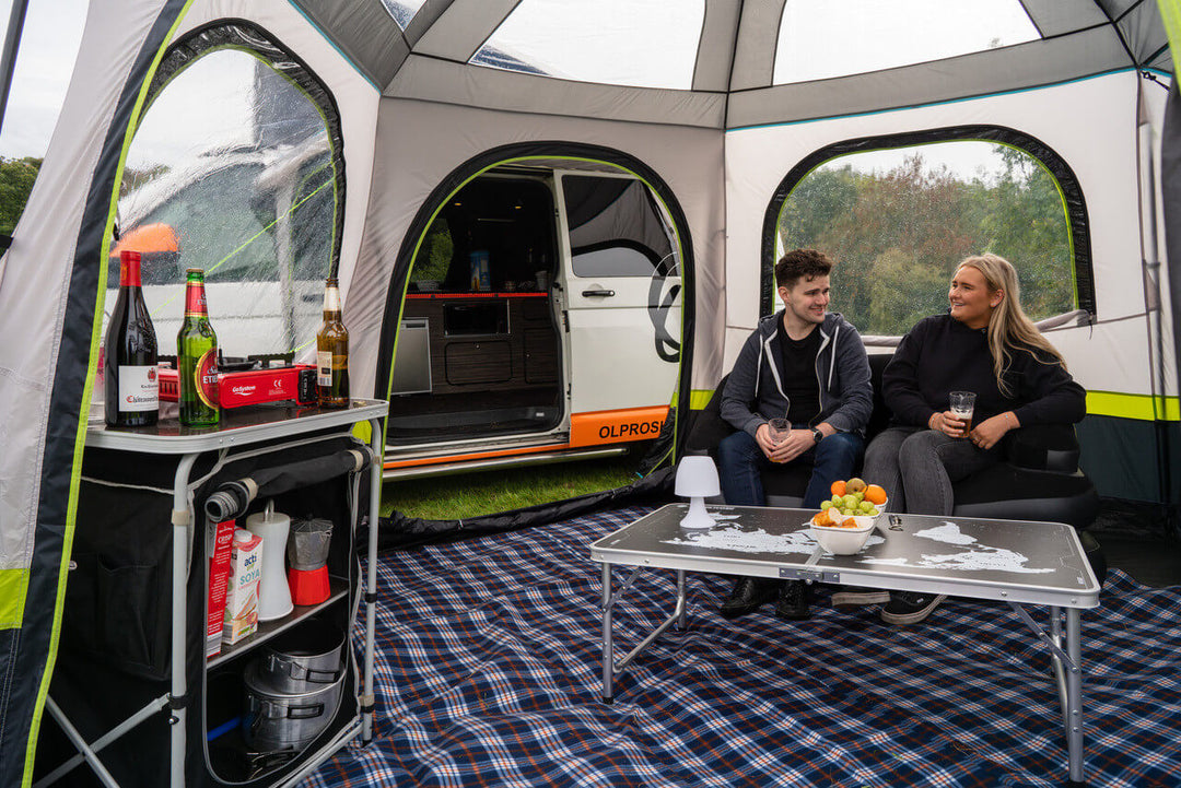 Interior view of the OLPRO Hive Campervan Awning showing people sitting inside with drinks on a campsite.