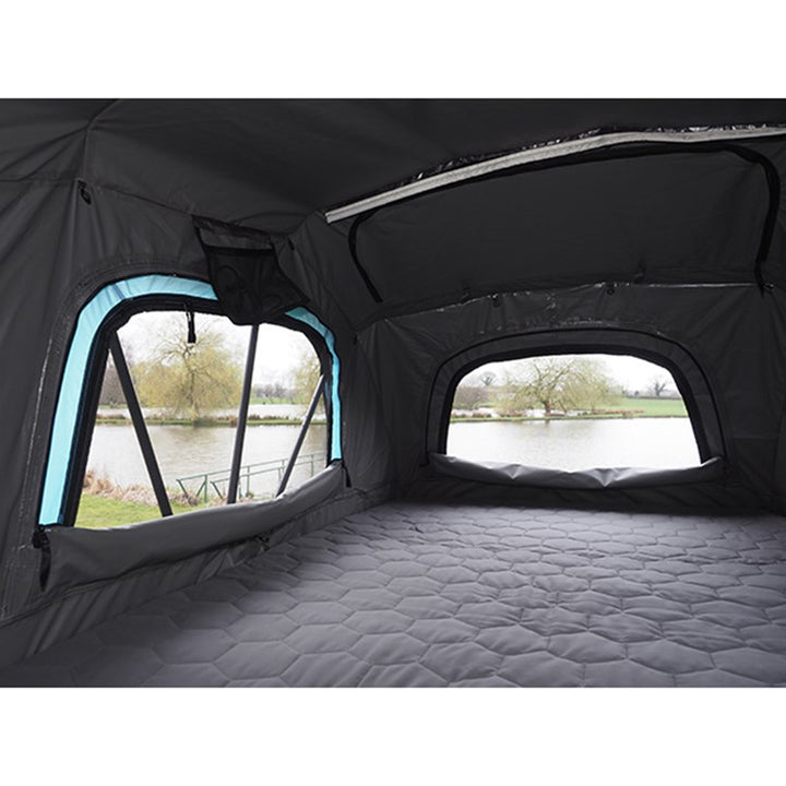 Interior of Skypod Lite rooftop tent showing spacious sleeping area and mesh windows overlooking a lake.