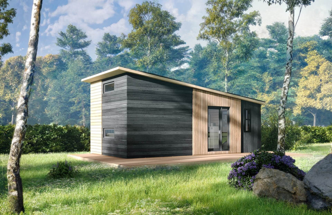 Modern cabin set in a grassy forest clearing, with black charred timber cladding and natural wood front panels.