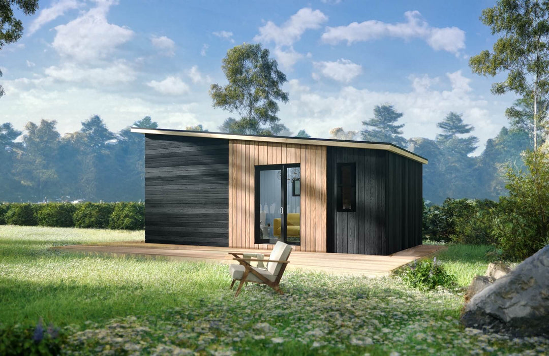 Angle view of a tiny home in a lush outdoor setting, showing its clean wood-clad exterior and a single lounge chair outside.