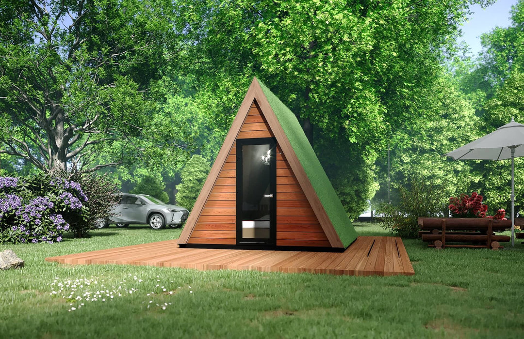 Front view of an A-frame glamping pod with black-framed glass door, parked car and purple flowers visible in the background.