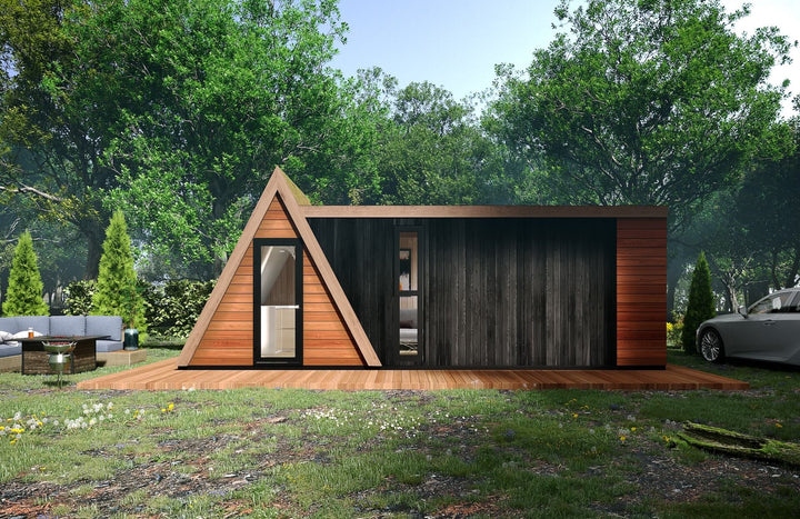 Clear front view of the hybrid glamping pod with black panel siding and an A-frame entrance, nestled in a wooded outdoor area.