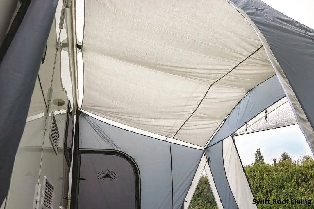 SunnCamp Swift Air 325 SC awning with a large clear front window, grey fabric panels and a black groundsheet attached to a white caravan.