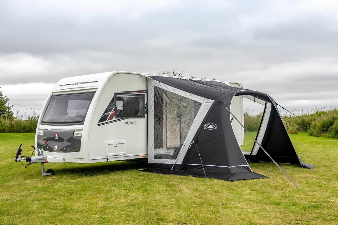 Black and grey SunnCamp 325 Air caravan awning with a large open front entrance, attached to a white caravan on a grassy campsite under an overcast sky.