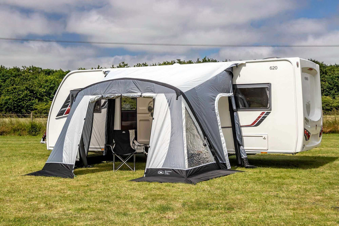 SunnCamp Swift Air 220 SC caravan awning with an open entrance and extended sun canopy, attached to a white caravan, set on a green campsite surrounded by hedges.