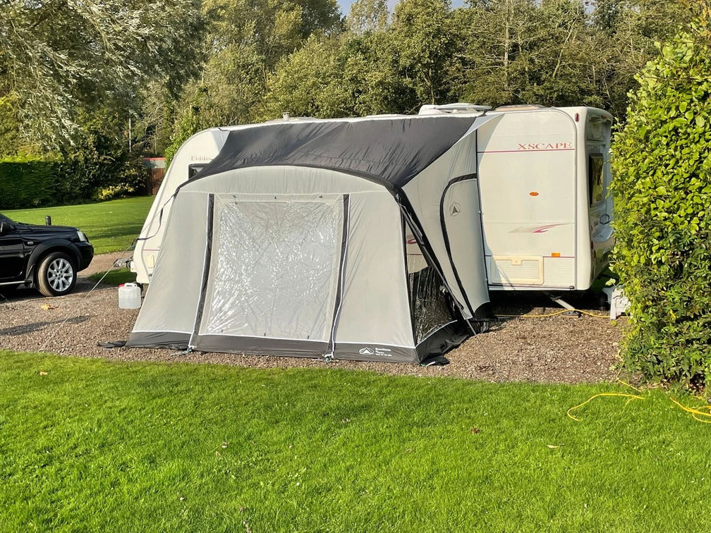 SunnCamp Dash Air 260 SC awning with a closed front entrance and clear window panel, attached to a white caravan in a sunny campsite.
