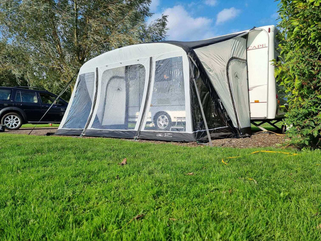 SunnCamp Dash Air 390 SC awning viewed from the front side, featuring clear PVC windows, black trim and an enclosed entrance beside a white caravan.