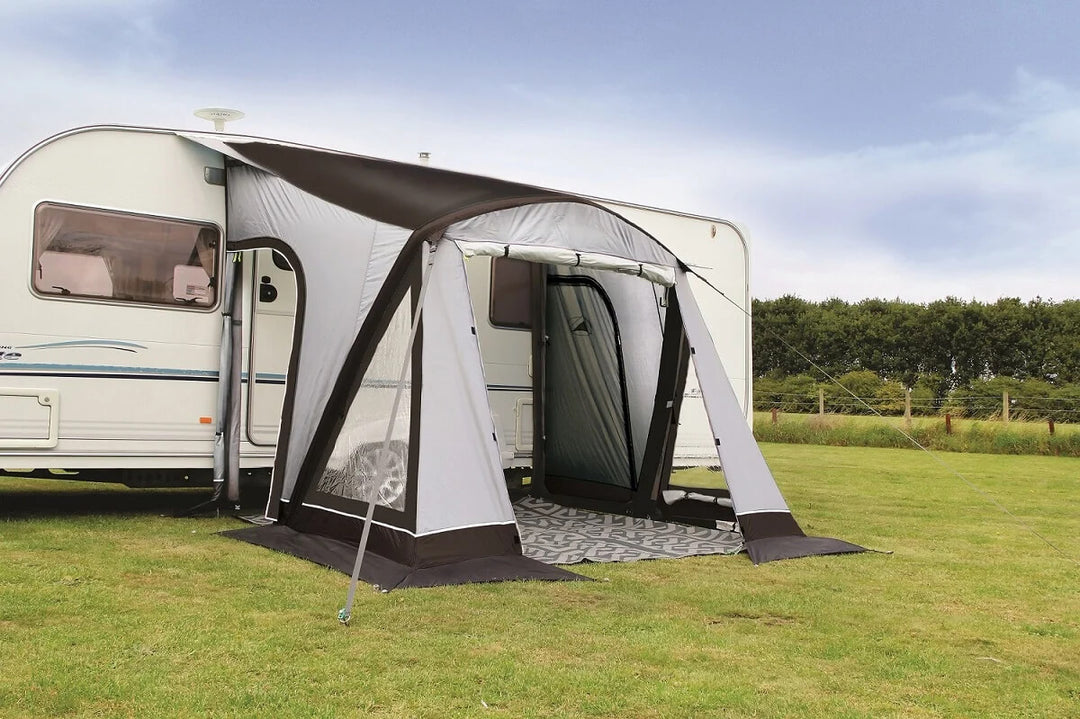 SunnCamp Dash Air 220 SC inflatable caravan awning attached to a white caravan, featuring grey and black fabric panels, a front entrance, clear side windows and a patterned groundsheet on a grassy campsite.