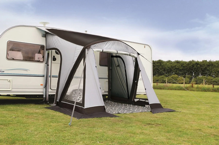 SunnCamp Dash Air 260 SC inflatable caravan awning attached to a white caravan, featuring grey and black fabric panels, a front entrance, clear side windows and a patterned groundsheet on a grassy campsite.
