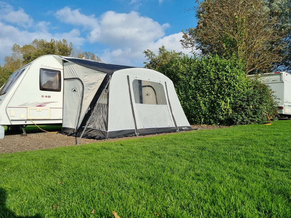SunnCamp Dash Air 260 SC awning attached to an Elddis caravan, viewed from the side with grey panels, clear windows, and a black base on a grassy campsite.
