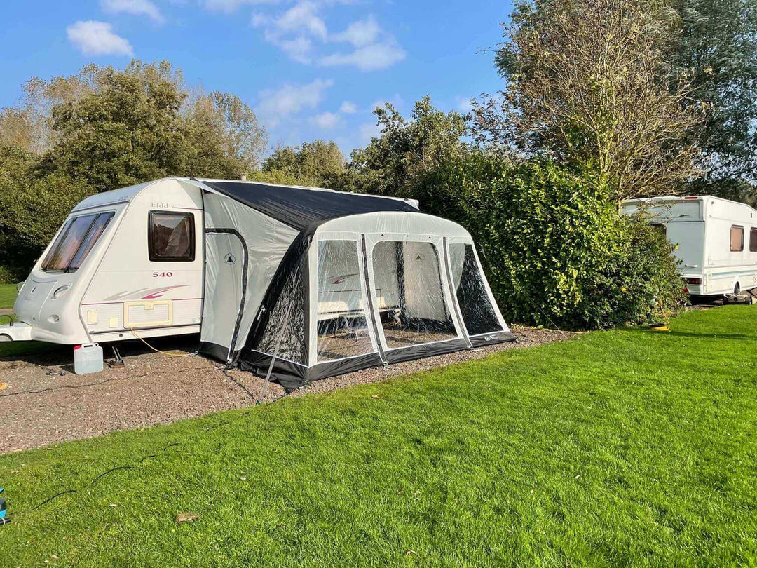 SunnCamp Dash Air 390 SC inflatable caravan awning with its front and side panels visible, set up on a gravel pitch surrounded by green grass and trees.