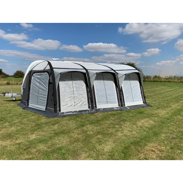 A Sunncamp Icon Air Awning displayed in its full length, showing four connected chambers with black support structures and white panels, attached to a caravan on mowed grass