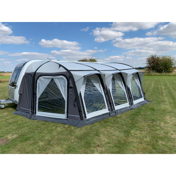 A Sunncamp Icon Air Awning photographed from a three-quarter angle, showing the full length of four sections with black air beams and white panels against a pastoral background