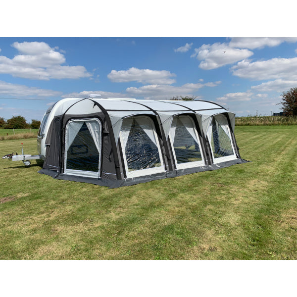 A Sunncamp Icon Air Caravan Awning shown from a side angle, featuring four interconnected sections with clear windows and black framework, positioned on a grassy field